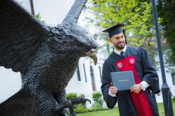 Recent graduate of Montclair State business school in front of hawk statue on campus