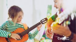 Little girl playing guitar with male teacher