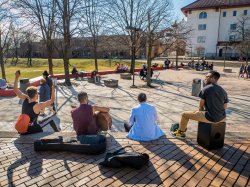 Students sitting in the quad on a sunny day playing guitar