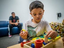 photo of young boy playing with blocks in foreground and an adult blurred in the background