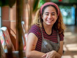 Student Samantha Wilk is photographed smiling while seated in a sunny hallway