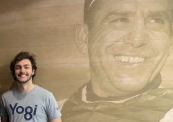 photo of Griffin Shoemaker standing against a wall backdrop of a sepia-toned photo of Yogi Berra smiling