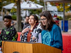 Student at microphone reading Land Acknowledgement with other students standing to her right