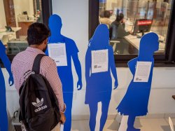 "A man stands in front of blue cardboard cutouts that represent survivors of human trafficking."