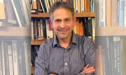 photo of David Galef standing with arm crossed in front of a filled bookshelf