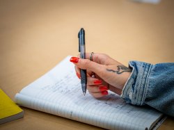 "A close up photo of hand with red fingernails holding a pen while taking notes."
