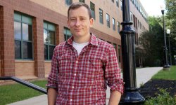 photo of man in plaid shirt standing outside of a brick building