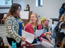 "Isabella Zarate Gonzalez and Associate Professor Pascale LaFountain, wearing SPARK T-shirts and ID lanyards, confer at the front of a classroom, holding worksheets."