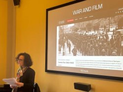Teresa Fiore stands at podium giving presentation with a projected slide visible behind her