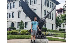 Noah Festerling stands next to the Red Hawk statue on campus