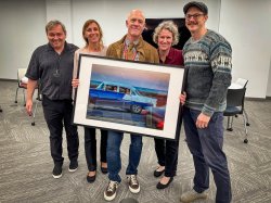 a group stands together with person in the middle holding a large photograph