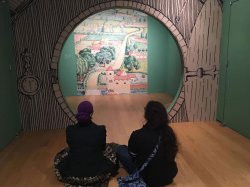 photo of two students sitting on floor in front of round door opening