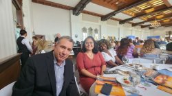 A professor sitting at a table with two of his students. Everyone is smiling and dressed professionally.