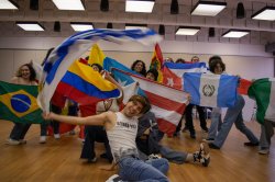 Students holding up flags from around the world, while smiling and standing and sitting in two rows.