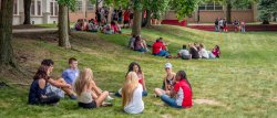 Photo of small groups of students sitting on campus green during orientation.