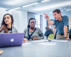 professor pointing at whiteboard while talking with students