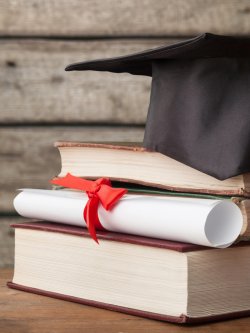 Image of a stack of books with a diploma and a graduation cap.