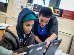 A social worker and a teenager collaborate in front of laptop