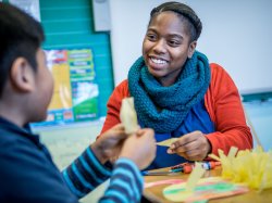 Woman social worker wearing with a young child in a classroom working on an arts and crafts project