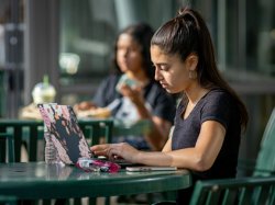 Woman student using laptop in outdoor seating area of cafe diem