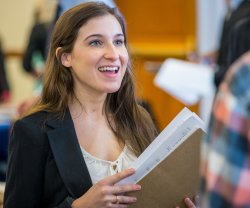 Woman in business attire holding notebook while talking with someone off-camera