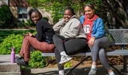 Three women students sitting on bench on the quad on a warm spring day