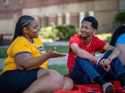 Two Bloomfield students sit on a blanket on the quad having a light-hearted conversation