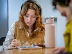 A student in a lounge reviews notes on an iPad while listening to music on headphones