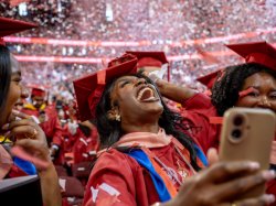 A woman in a red graduation cap and gown at commencement celebrates under a shower of confetti