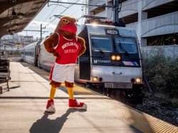 Mascot, Rocky, standing on the platform of the train station as a train approaches.