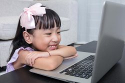 Little girl wearing pink bow using laptop.