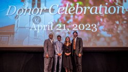 Four people stood on a stage in front of projector screen reading Donor Celebration, April 21, 2023