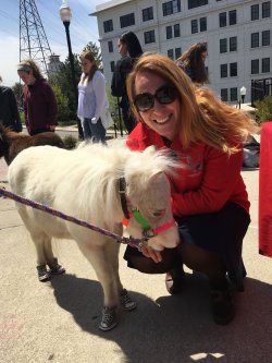 Marie Cascarano outside on a sunny day with a white mini horse smiling