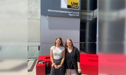 Drs. Nina Kaiser and Daniela Peterka-Benton stand for a photo together outside. A sign for Universit Graz is behind and above them