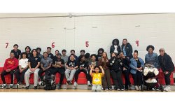 a large group of participants and families sits together in a gym for photo after soccer clinic