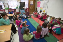 Photo children sitting on floor in a classroom listening to their teacher.