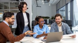 group of four people talking around a laptop
