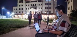 Student sitting on a bench with laptop at night