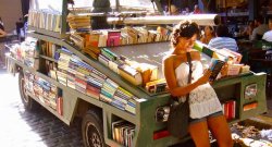 Woman leaning against truck turned into mobile library in a tropical country