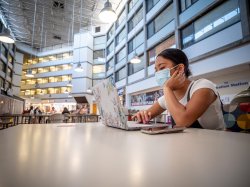 female student working on laptop wearing facemask indoors