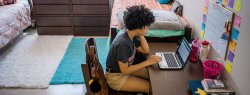 African-American female in dorm room at desk working on laptop