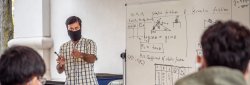 male faculty teaching to students with formulas on whiteboard