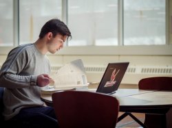 Student with papers and a laptop seated at a desk