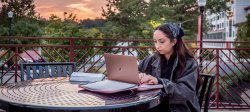 female student outdoors working on laptop in lounge type setting