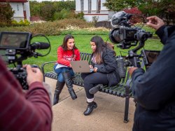 Two women getting filmed on bench.