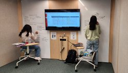 Two students writing on whiteboard wall in creative collaboration pod