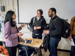 two students speaking to a professor in a classroom