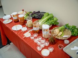 Baskets of cabbage and root vegetables and jars of Kimchi sit on a red table cloth