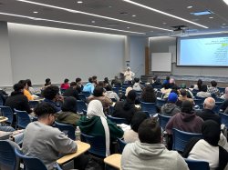 photo of full lecture hall-style room with presenter at front