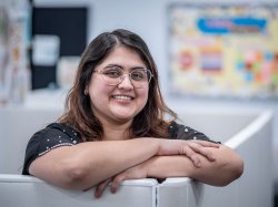 "Isabella Zarate Gonzalez leans on a white cubicle wall with arms crossed."